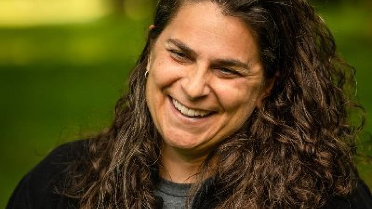 A woman with long brown curly hair mid-laugh.