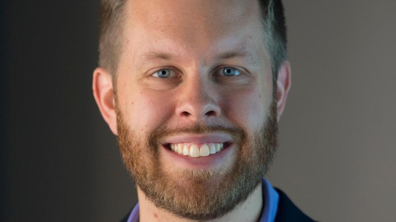 A man with blond hair and beard smiles.