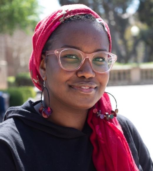 A woman with glasses and a red head scarf smiles in the sun.