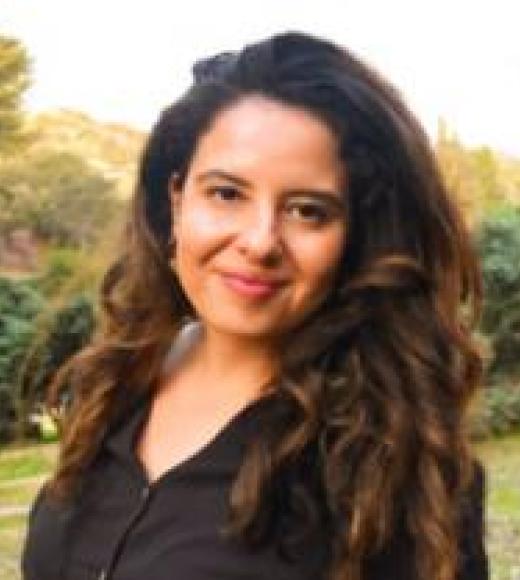 A woman with long, curly hair smiles outdoors.