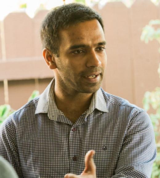 A man with short dark hair in a shirt in conversation.