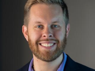 A man with blond hair and beard smiles.