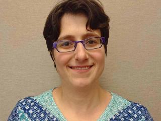 A woman with short hair, glasses and patterned shirt.